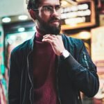 Portrait of a stylish man with glasses in an urban street setting, showcasing modern fashion.